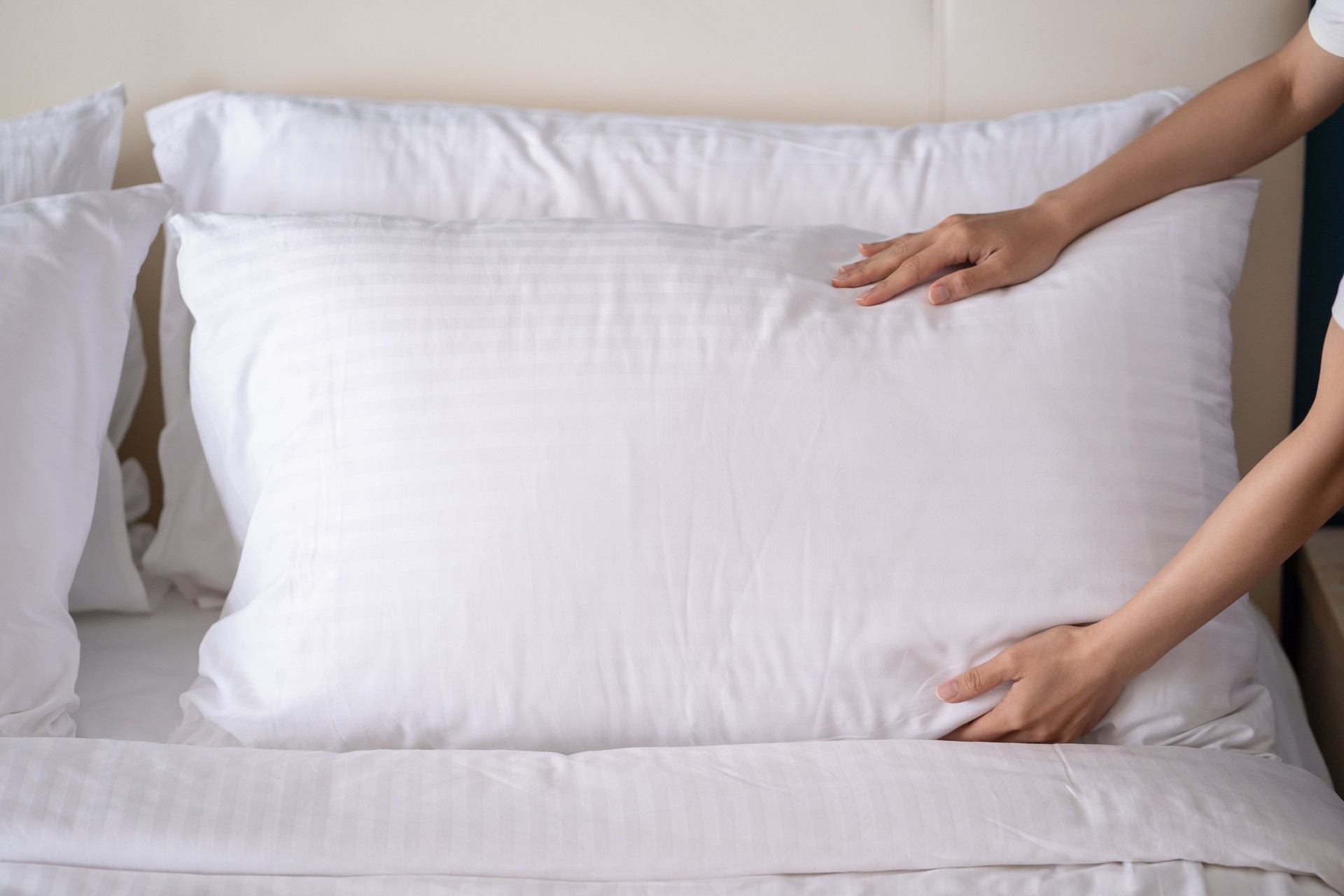 Las manos de una mujer asiática colocando una almohada blanca sobre una cama. Servicio de habitaciones del hotel. Mantenimiento de la casa